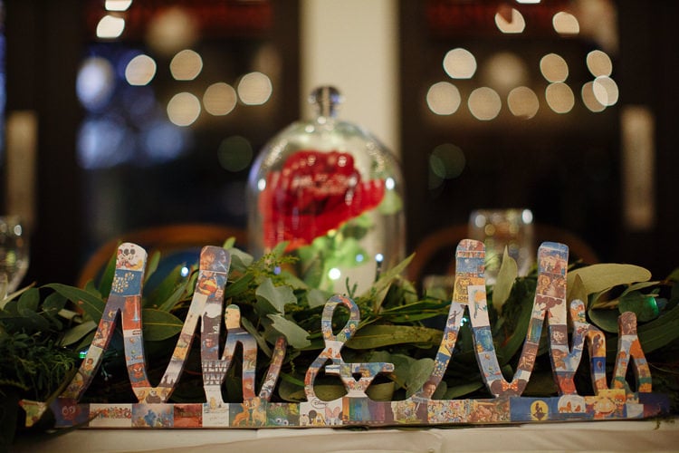 A collage-covered Mr & Mrs sign sits among foliage beside a rose under glass at Sunnybrae Estate.