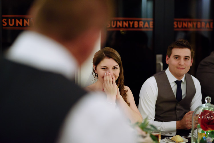 Shannon covers her mouth laughing beside Luke at the bridal table, Sunnybrae lettered on the doors behind.