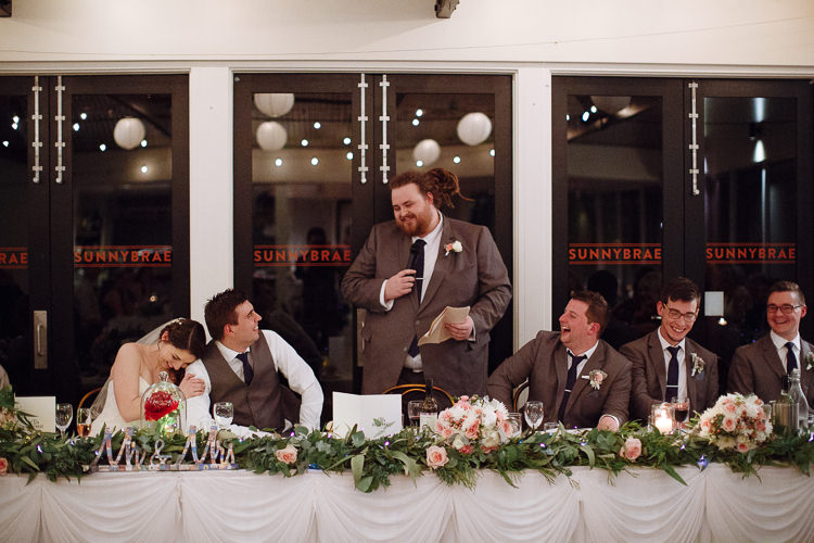 A groomsman gives a speech as Shannon leans against Luke laughing at the bridal table at Sunnybrae Estate.
