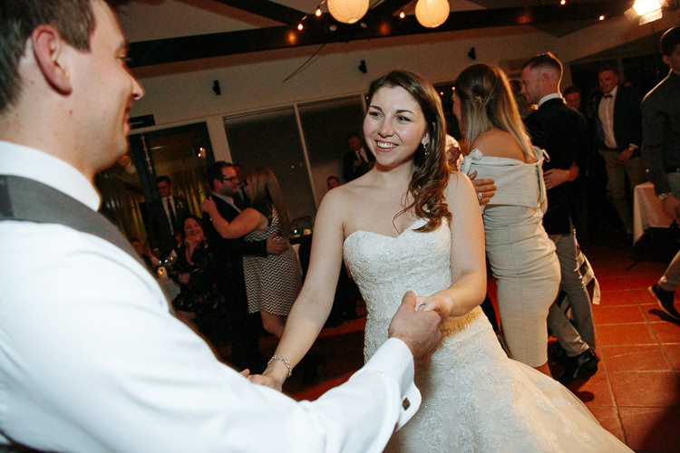 Over Luke's shoulder, Shannon smiles at him holding both his hands on the dance floor.