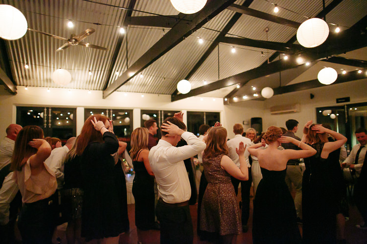 Guests dance with matching raised-arm movements beneath lanterns and festoon lights at Sunnybrae.