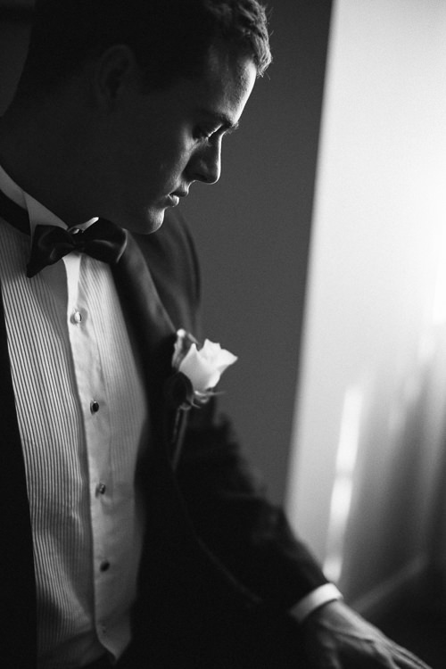 Head bowed in monochrome, white rose bright on the lapel