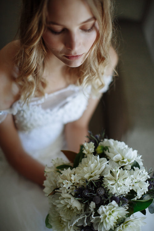 From above, the woman's lashes settle as she looks down over the white dahlia bouquet.