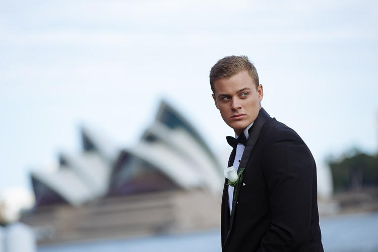 A man in a tuxedo looks back with the Opera House across Sydney Harbour.