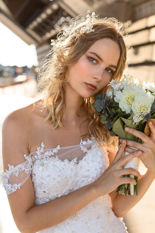A woman holds her bouquet against sandstone beside Sydney Harbour, beneath the bridge approach.