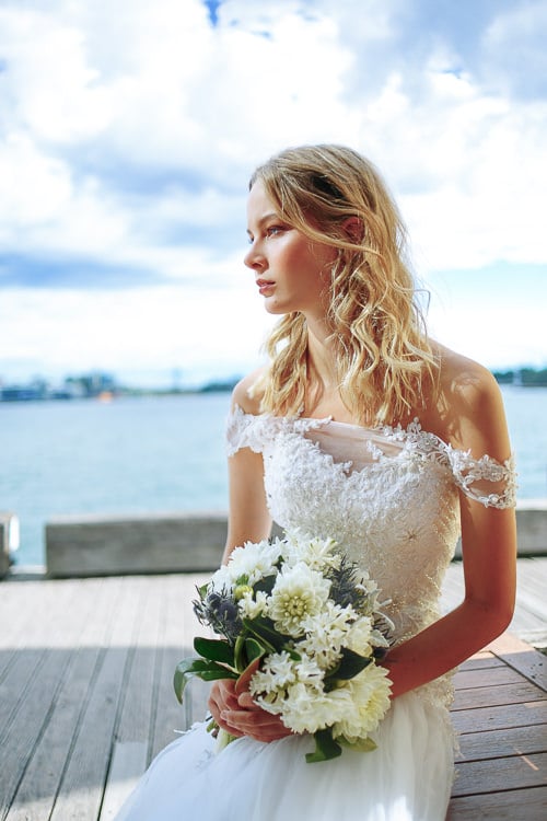 A woman sits with her bouquet on a Sydney Harbour timber platform, looking across the water.