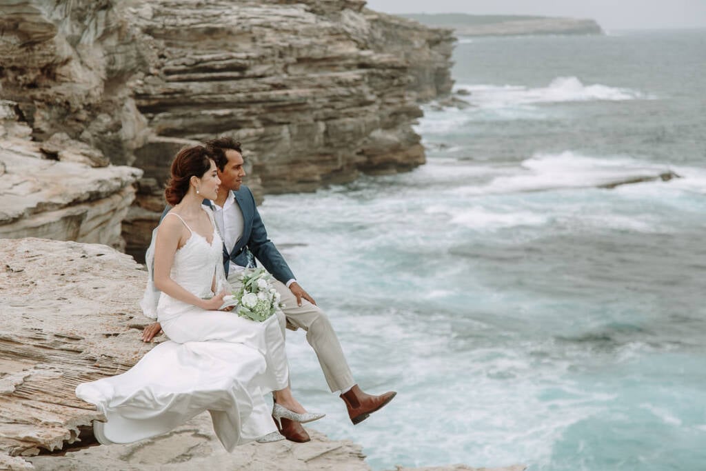 Jeannette and Pierre sit together on layered sandstone at Cape Banks, with white surf breaking below.