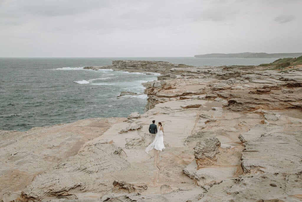 Wide view of Jeannette and Pierre on the sandstone headland at Cape Banks, with the sea to their left.