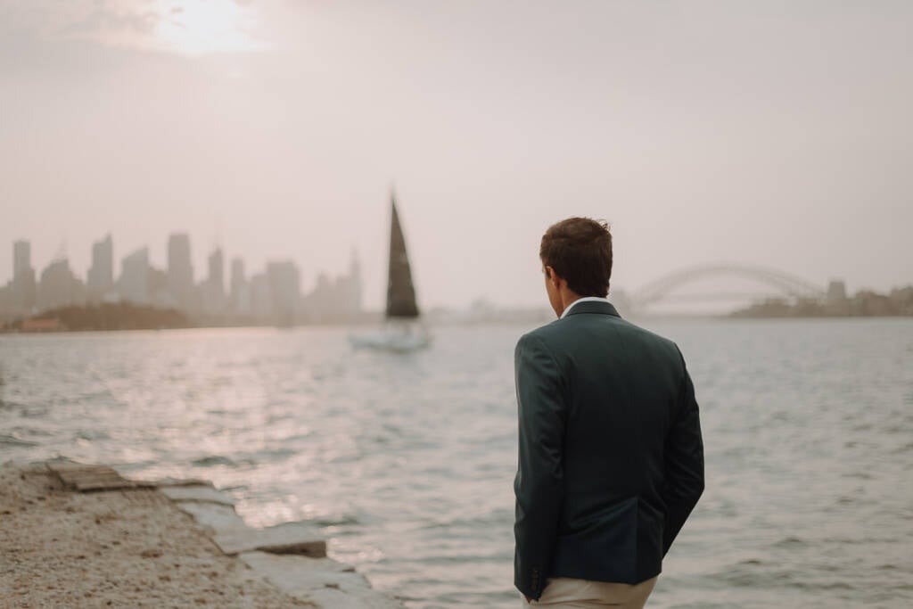 From behind, Pierre looks across Sydney Harbour from Bradleys Head as a sailboat crosses the water.