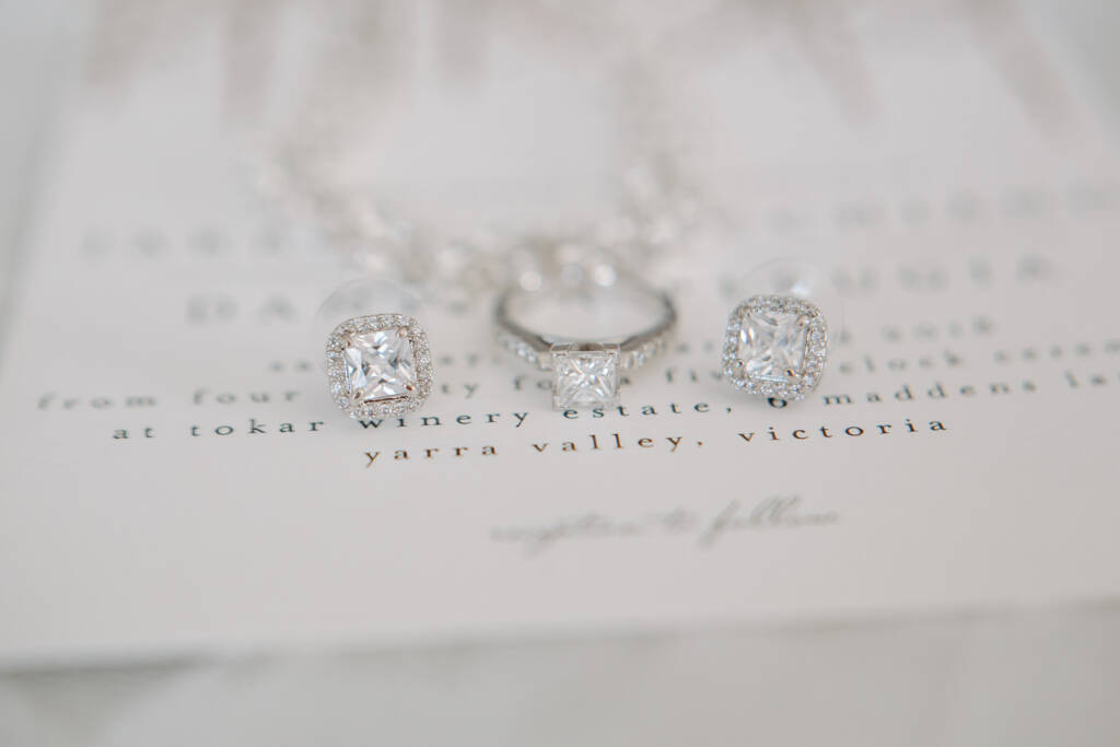 Halo earrings and the engagement ring rest on the lettered invitation
