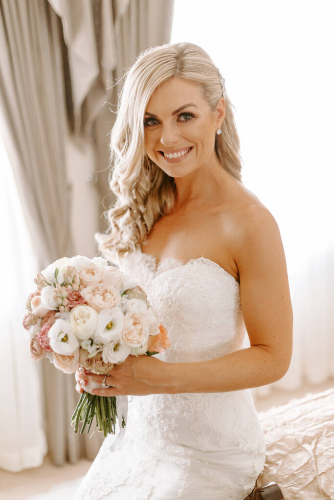 A radiant smile above the bouquet of blush garden roses, ranunculus and lisianthus.