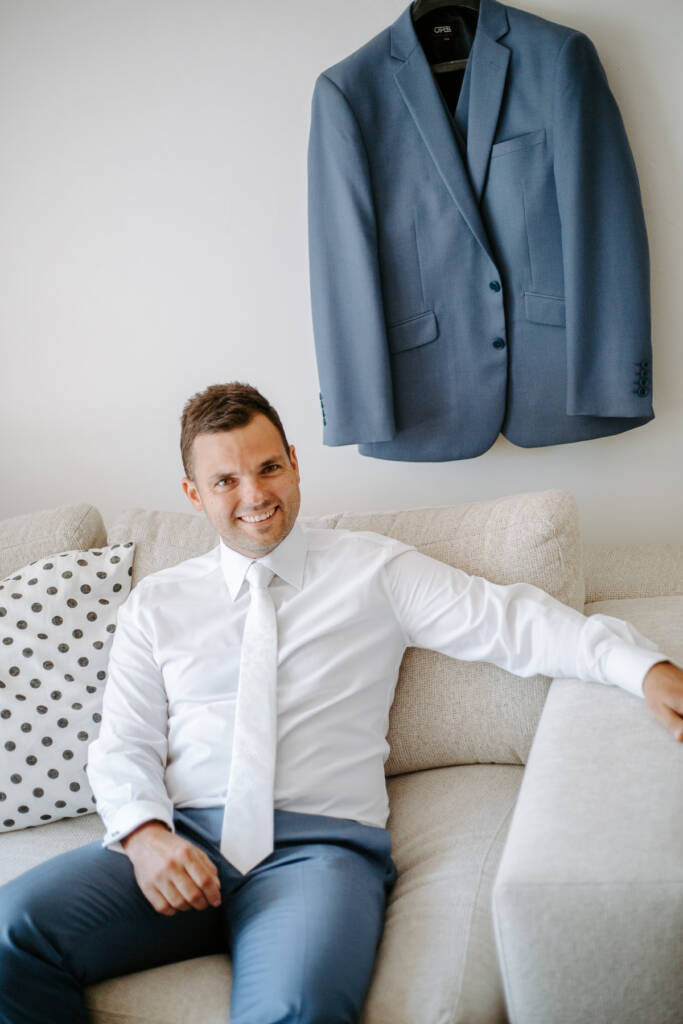 Relaxed on the couch in his ivory tie, steel-blue jacket hung above
