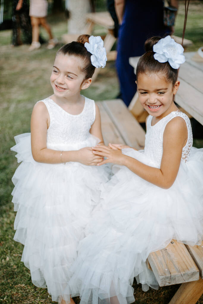 Two flower girls in ruffled tulle compare bracelets on the bench