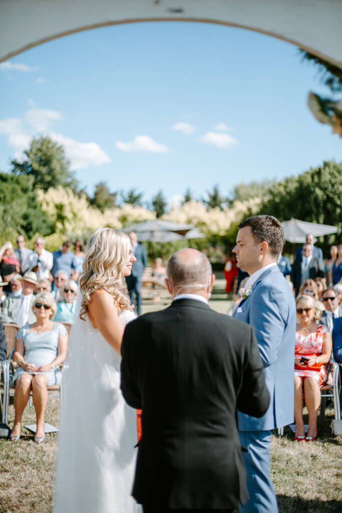 Danni and Jarrod face each other as their celebrant stands between them.