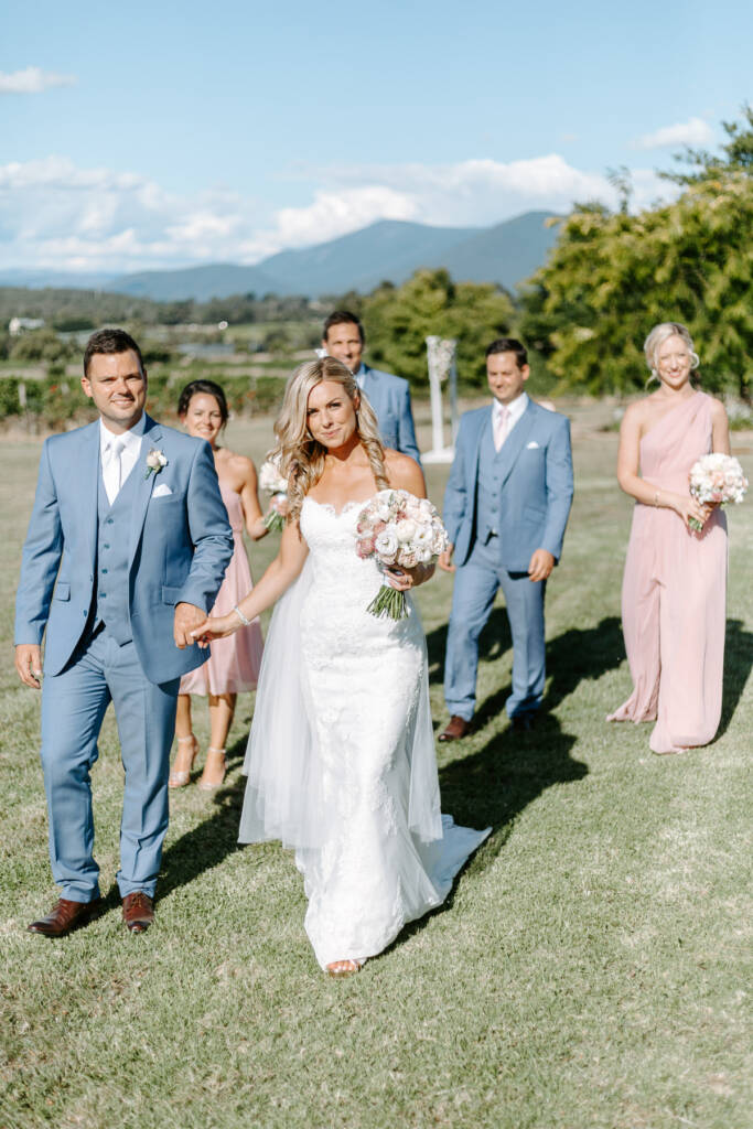The wedding party walks Tokar Estate Winery's lawn with the Yarra Ranges beyond.