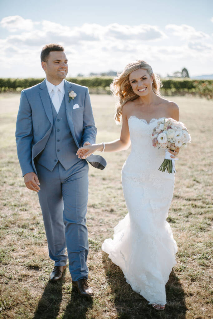 Danni and Jarrod walk together smiling, her bouquet held at her side.