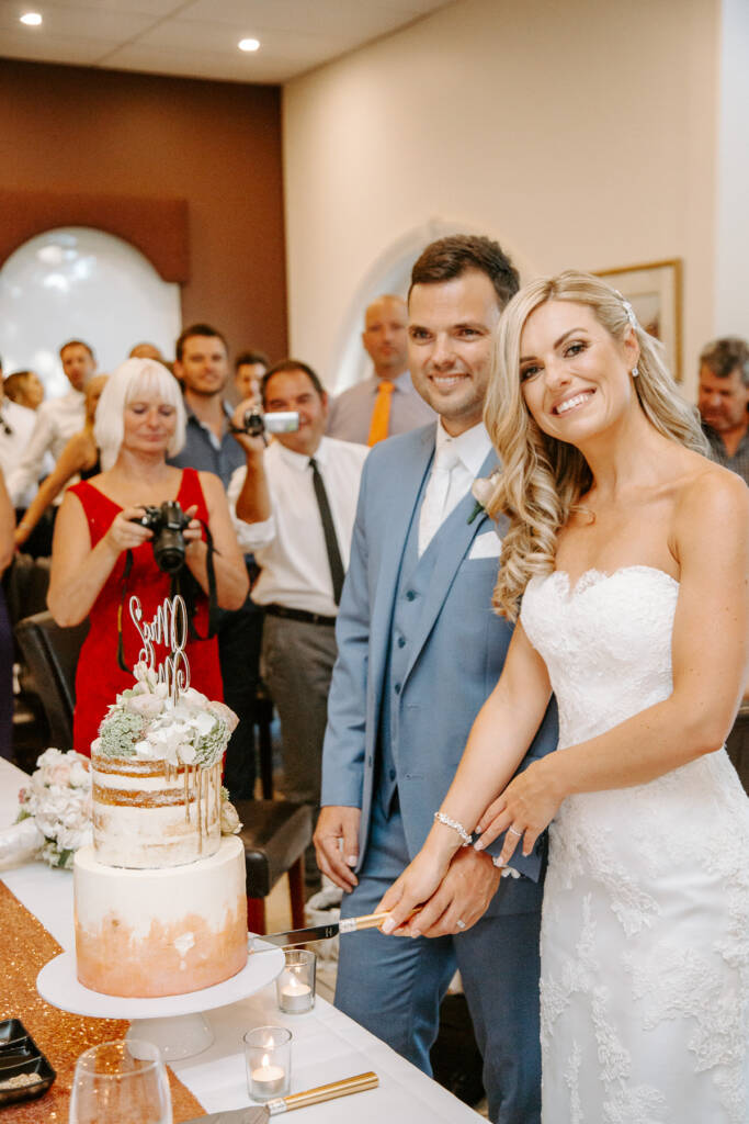 Danni and Jarrod cut their gold-drip wedding cake as guests take photos.
