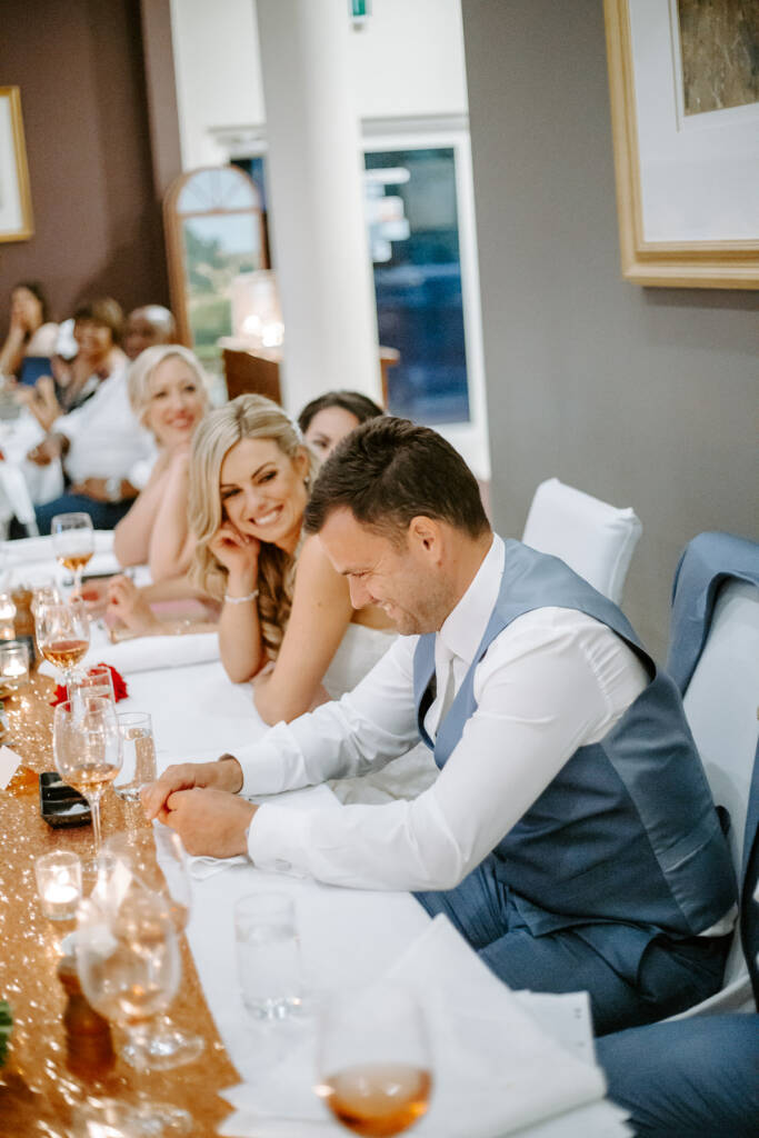 The groom cracks up mid speech while the bride and bridesmaids look on.