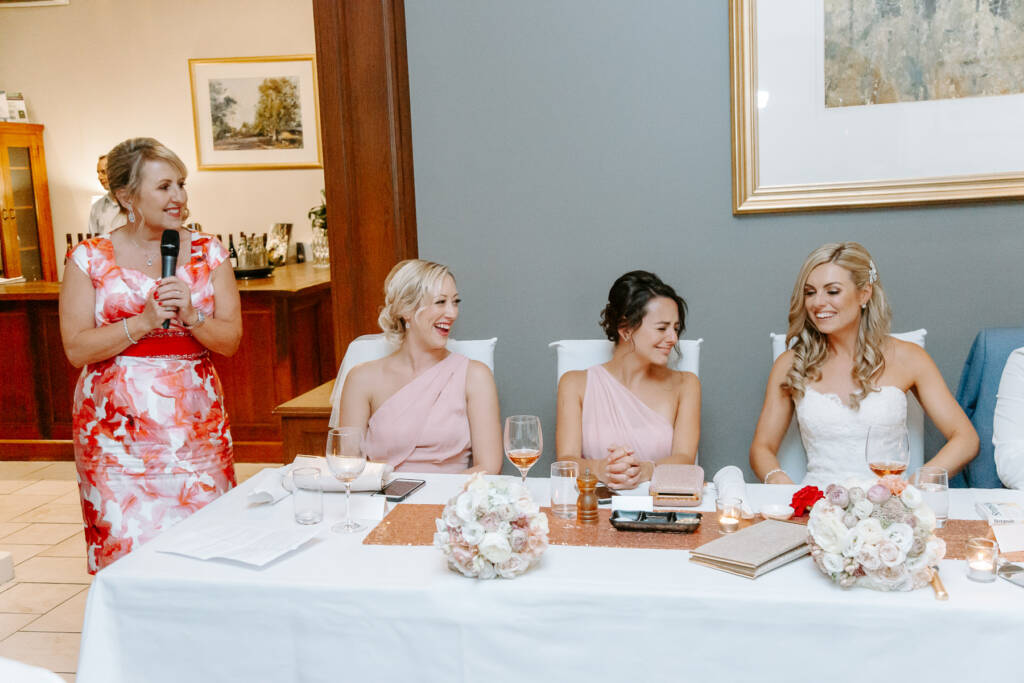 The woman in coral florals holds the microphone and the room's attention.
