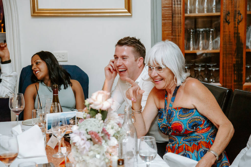 A guest in cat-eye glasses laughs and points towards another guest.