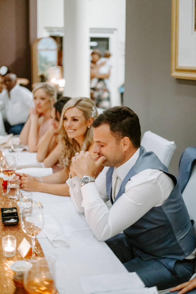 The groom bites a knuckle, caught between tears and laughter
