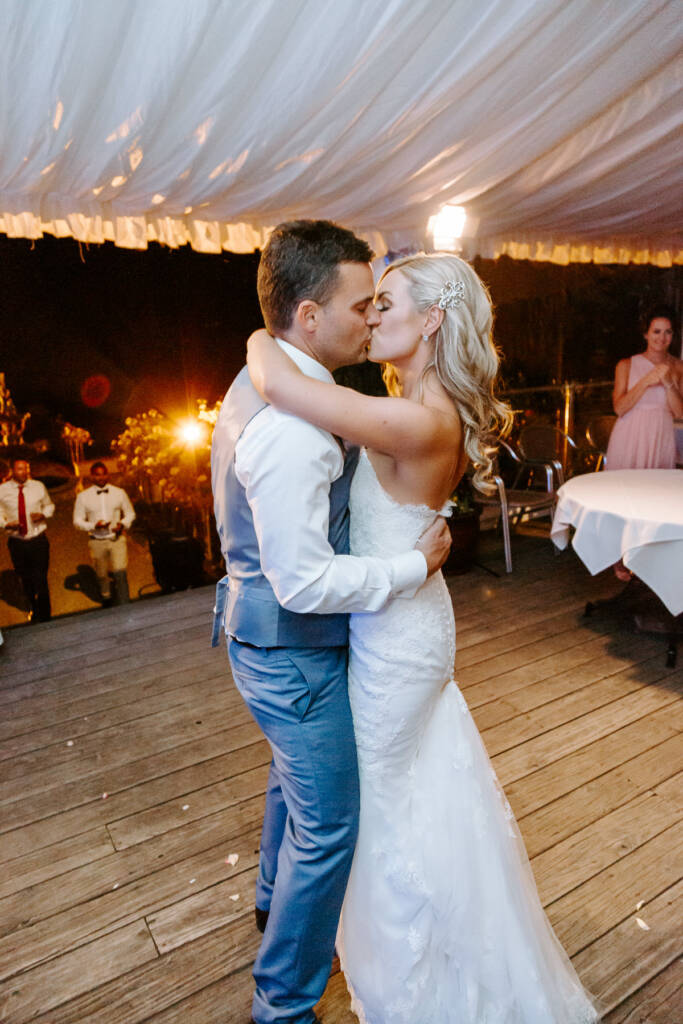 Danni and Jarrod kiss beneath Tokar Estate's marquee lights on the deck.