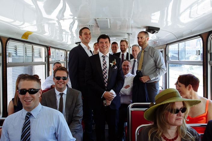 The whole crew packs the bus, Dennis grinning mid aisle, hats and sunglasses everywhere.