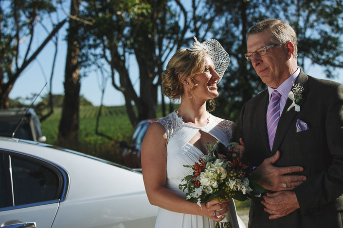 Lindsey on the arm of a silver haired man in a lilac tie by the white sedan.