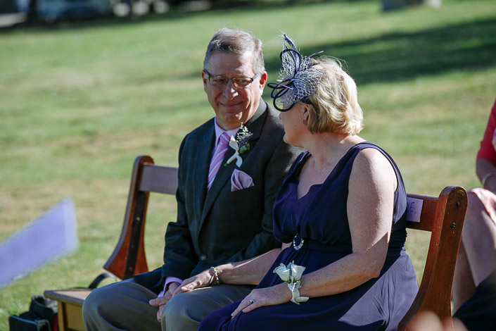 A man in a pink striped tie and Lindsey's mother in a navy fascinator smile from the bench.