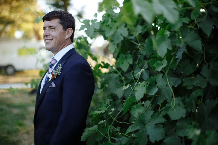 Dennis smiles into the distance beside the vine hedge