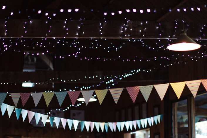 Pastel bunting criss-crosses under the fairy-lit rafters, a pendant lamp glowing at the edge.