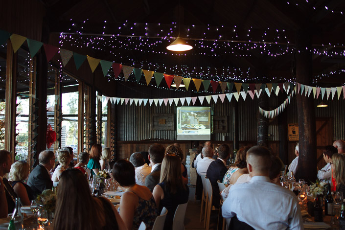 A slideshow plays above the bunting to the packed shed as the guests watch.