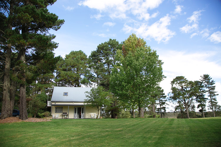 A pale cottage stands among tall trees on the lawn at Yester Grange Estate