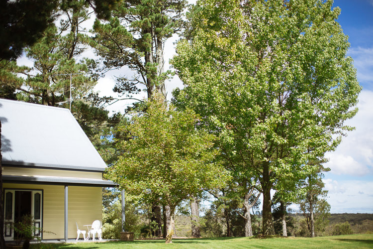 White outdoor chairs sit beside a cottage overlooking lawn and trees at Yester Grange Estate