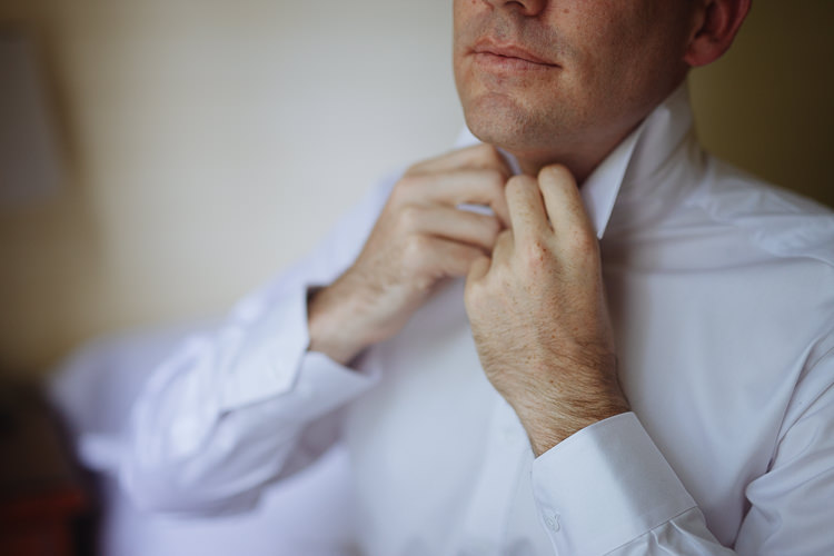 Close-up of Russell fastening the collar of his white wedding shirt