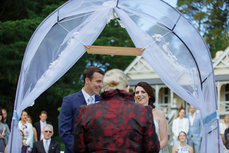 Heidi and Russell smile towards their celebrant beneath the arch at Yester Grange Estate