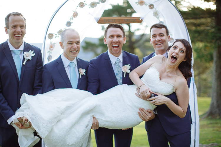 Russell and three groomsmen hold a laughing Heidi beside the ceremony arch at Yester Grange
