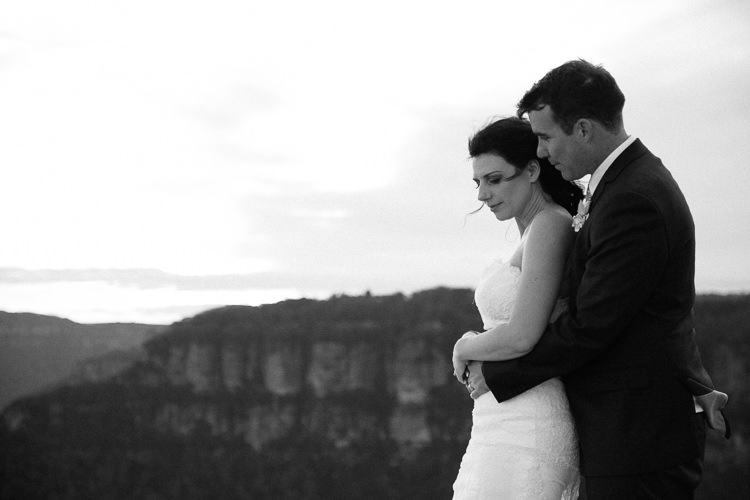 Black-and-white portrait of Heidi and Russell embracing with cliffs behind them at Lincoln's Rock