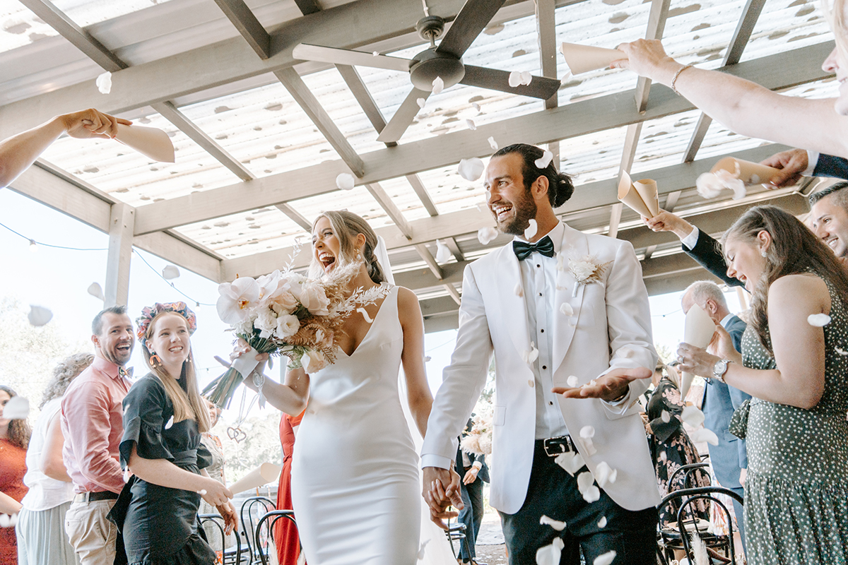 Petals fly as Jena and Matt make their exit through the pavilion at Barn and Co