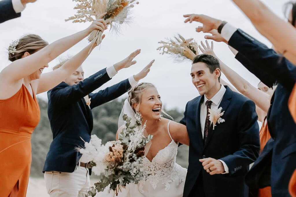 The bridal party arches dried-flower bouquets over Nina and Hayden at Gracelands, Forresters Beach