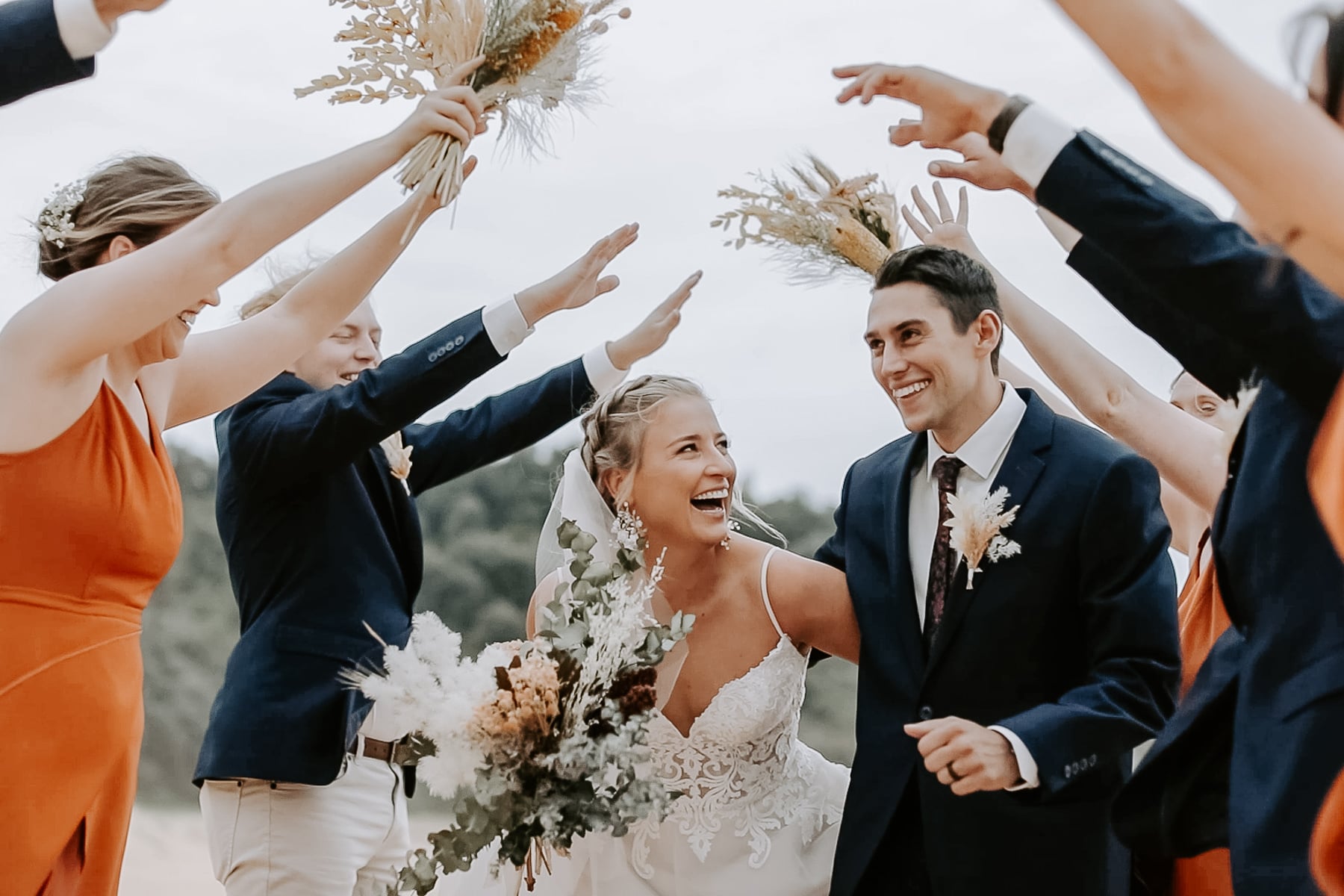 The bridal party arches dried-flower bouquets over Nina and Hayden at Gracelands, Forresters Beach