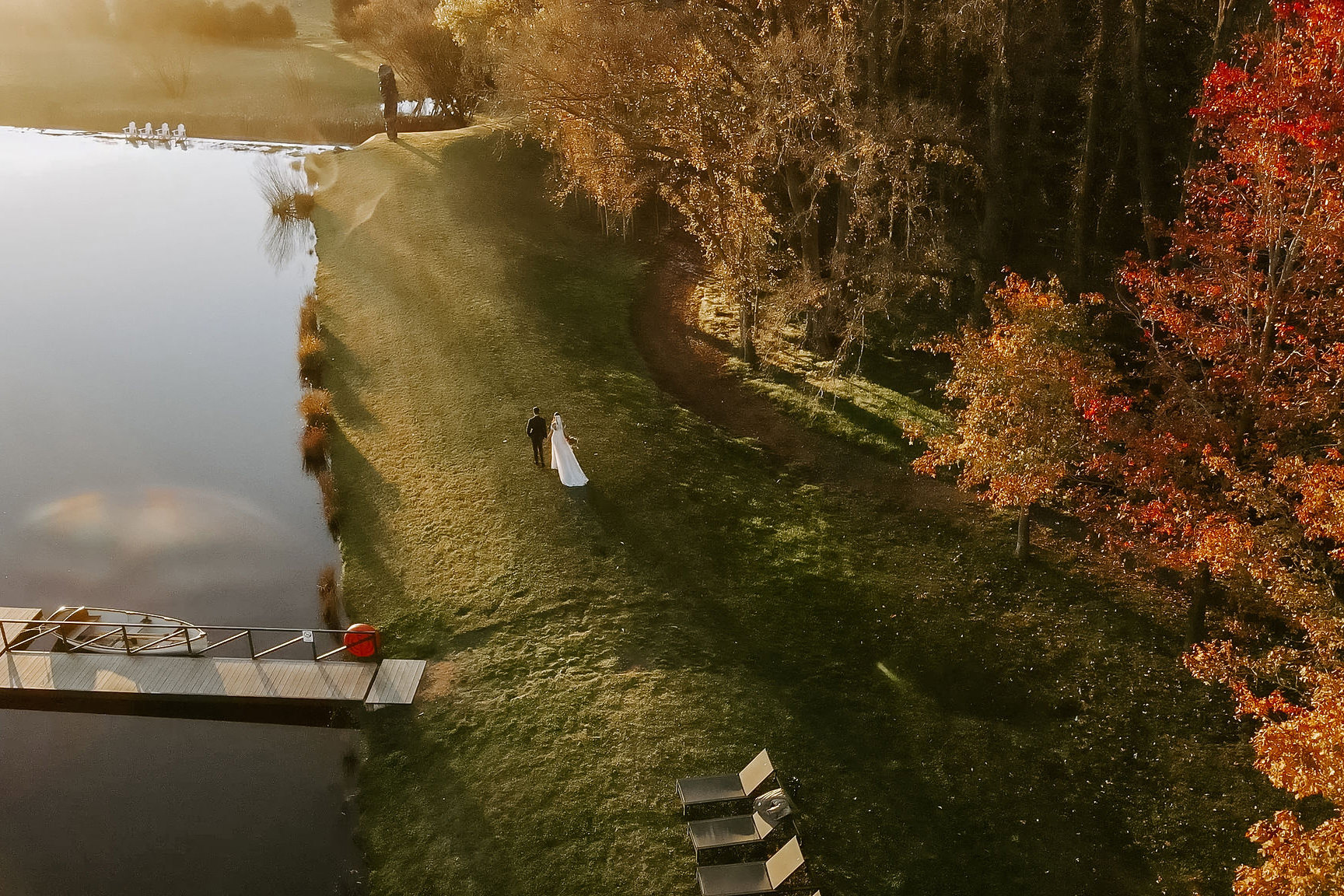 From above, Erica and Matthew cross the lakeside lawn in autumn light at Mona Farm, Braidwood