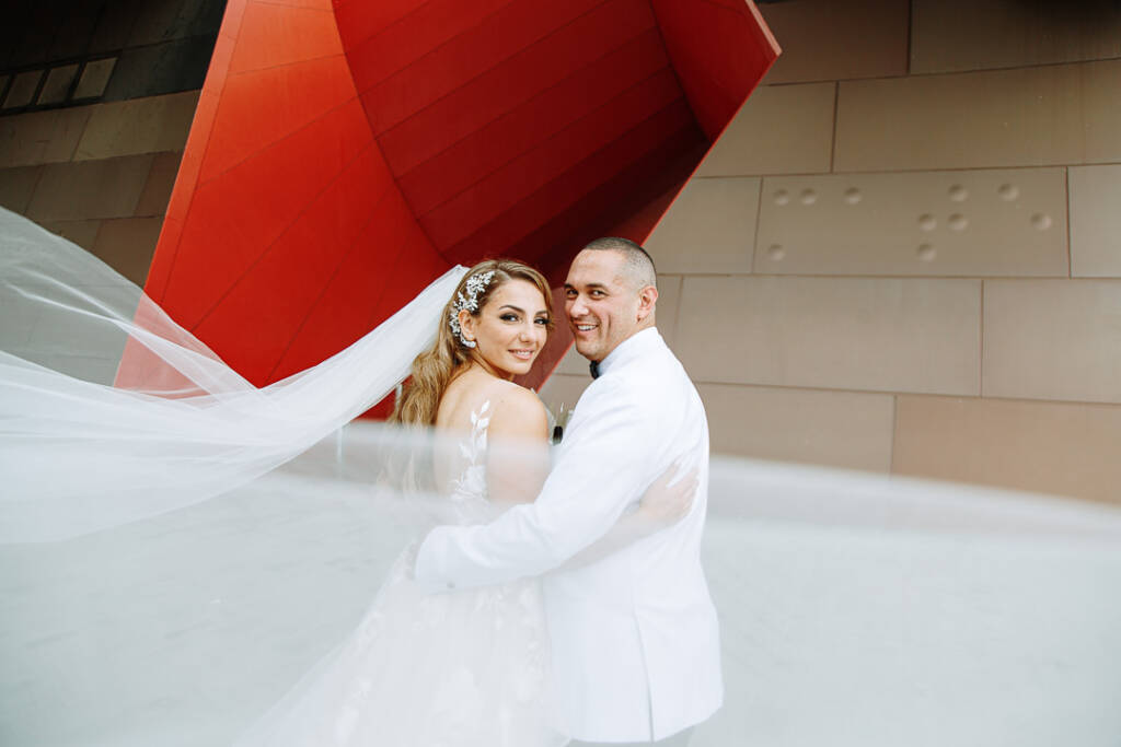 Trish and Chris beneath the red loop sculpture as the veil sweeps through, National Museum of Australia