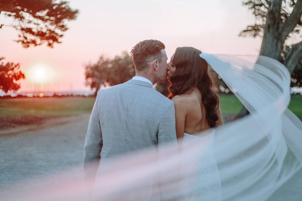 A veil sweeps around Georgia and Michael's sunset kiss in Catani Gardens, St Kilda