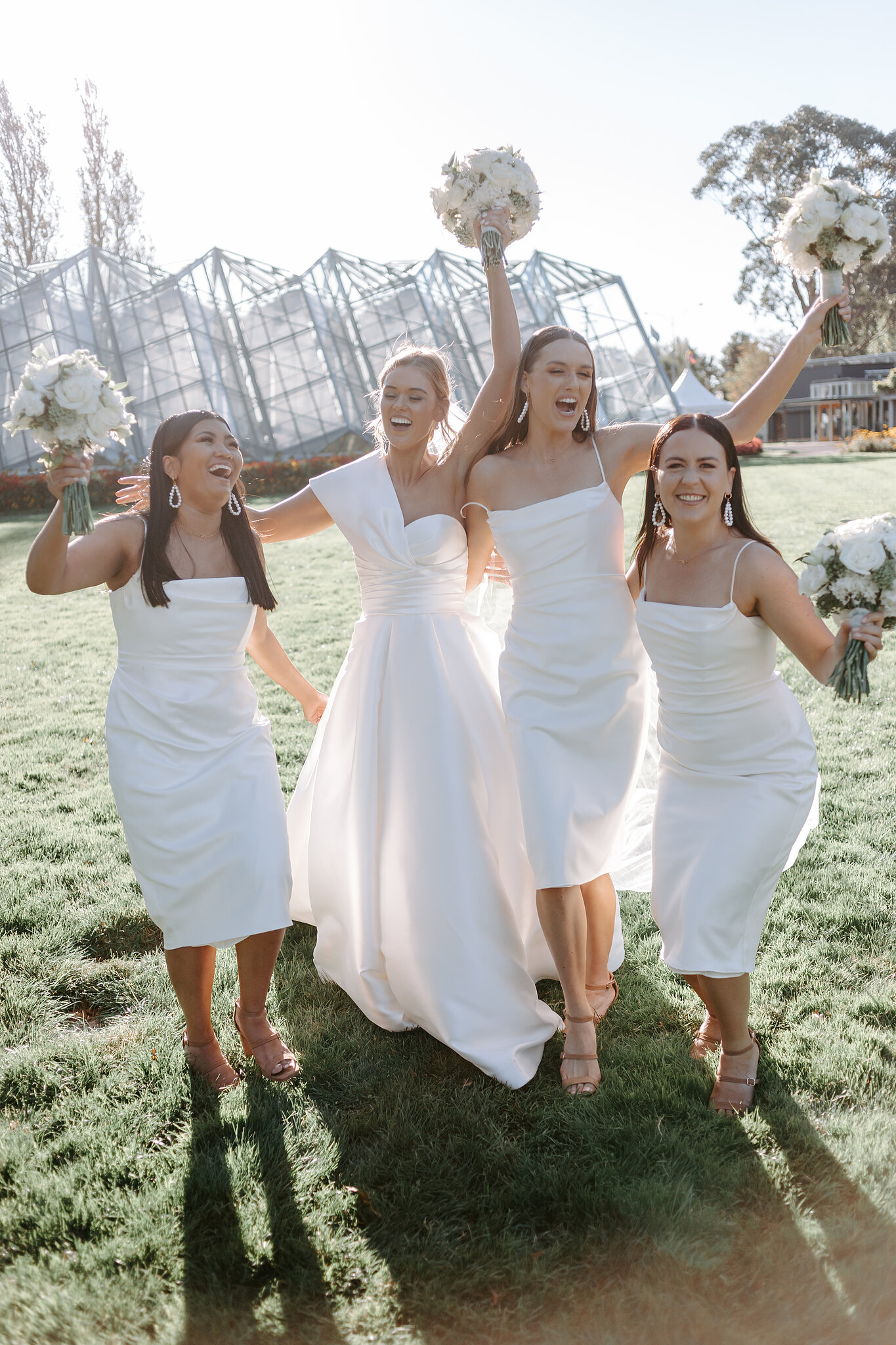 Georgie and her bridesmaids cheer with bouquets raised on the lawn at Ballarat Botanical Gardens.