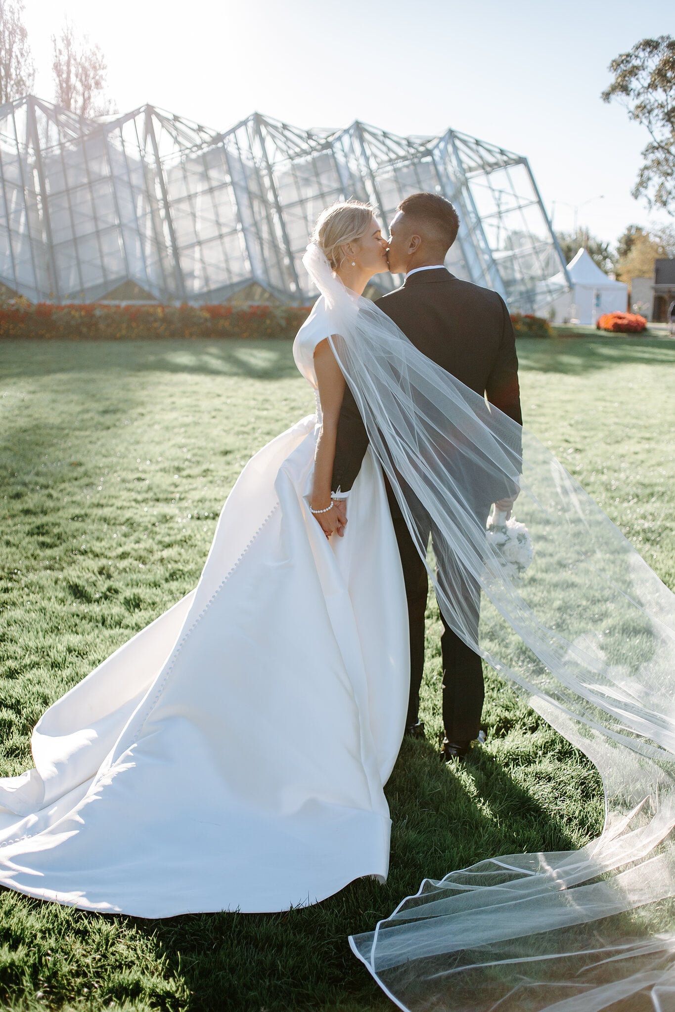 Georgie and Johnny kiss on the lawn, her veil trailing, before the Ballarat Botanical Gardens conservatory.
