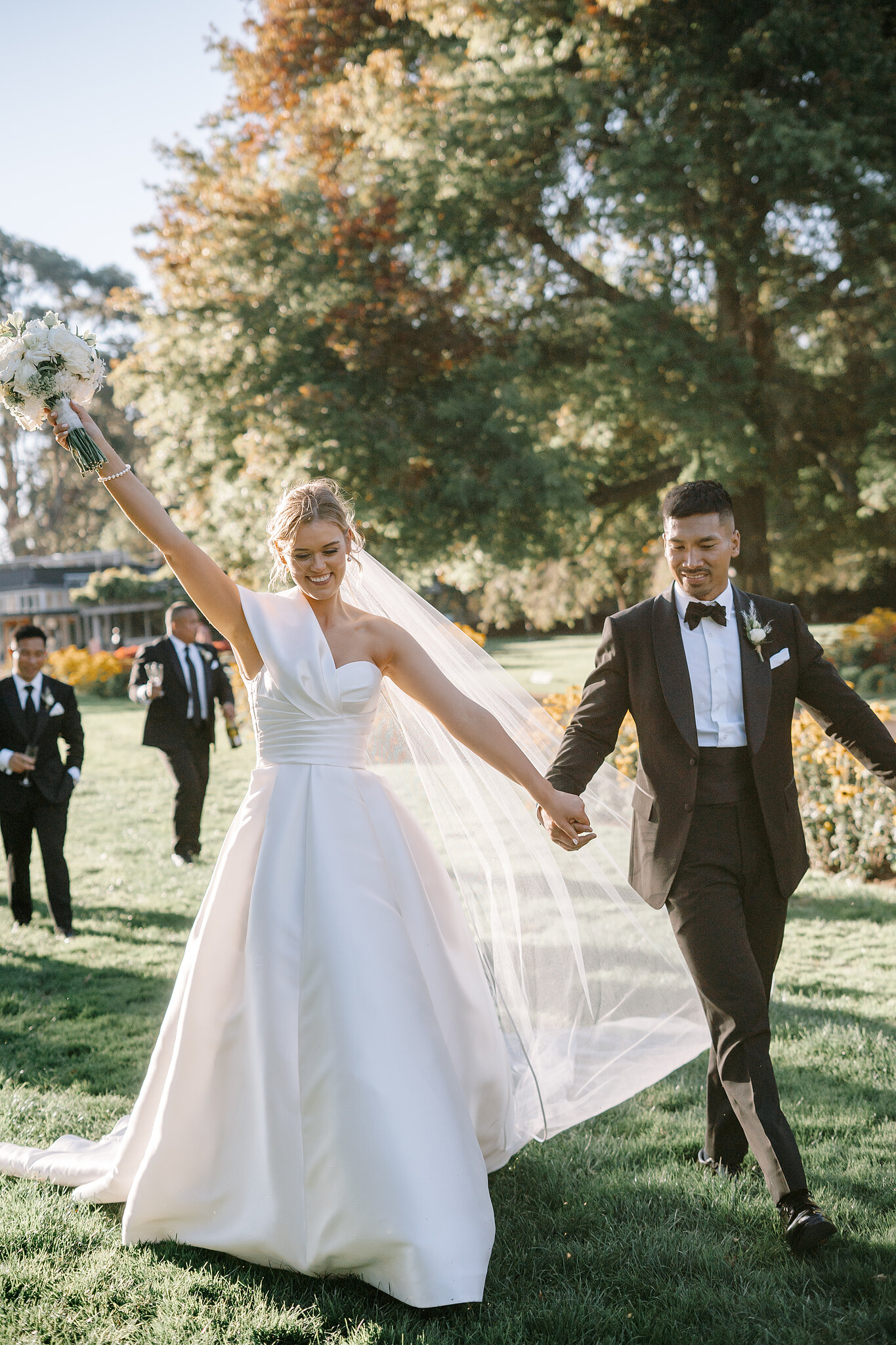 Georgie throws her bouquet skyward as she and Johnny cross the lawn, groomsmen close behind.