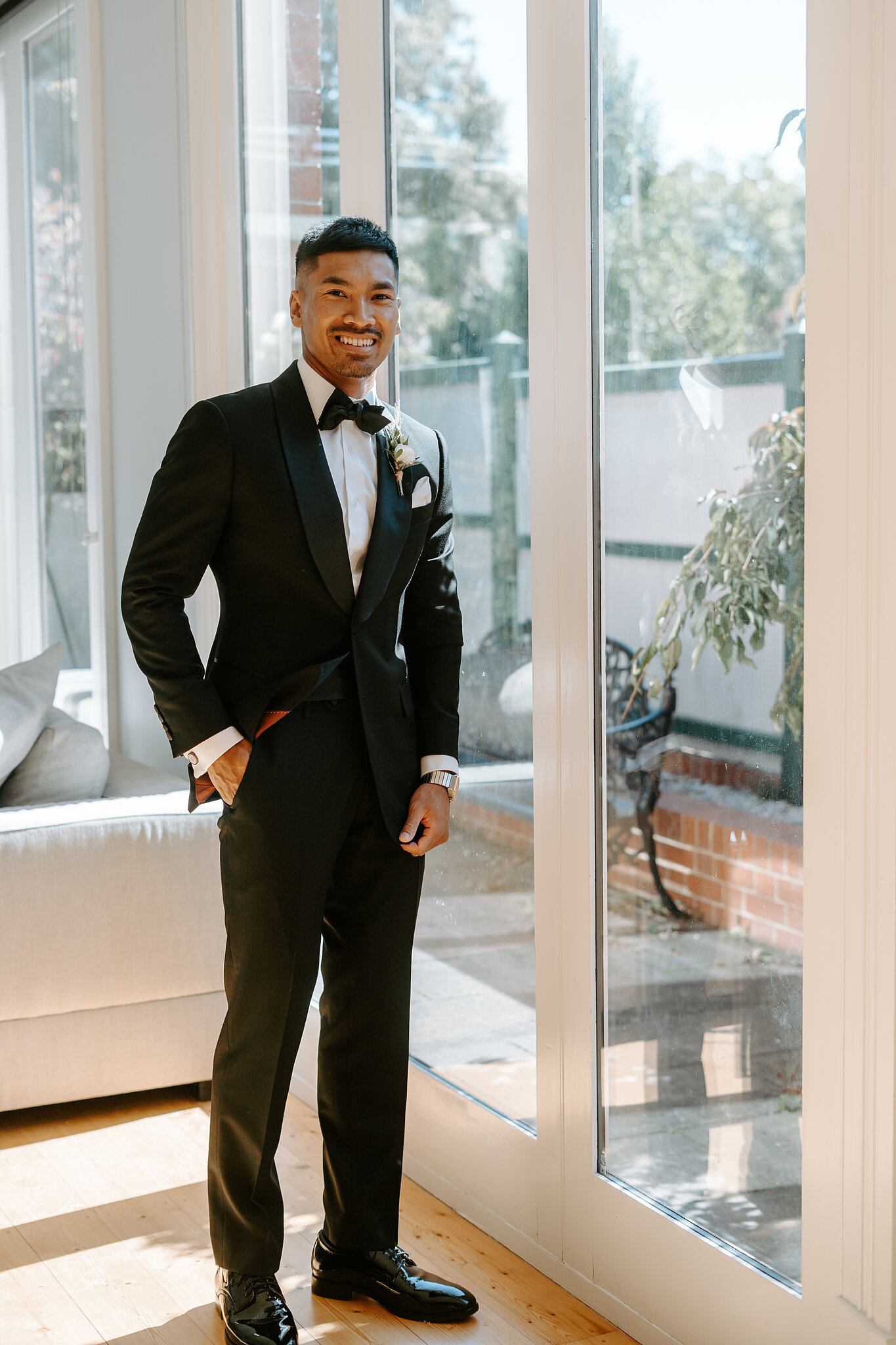 Johnny stands by sunlit glass doors, hand in pocket, ready to leave for the ceremony.