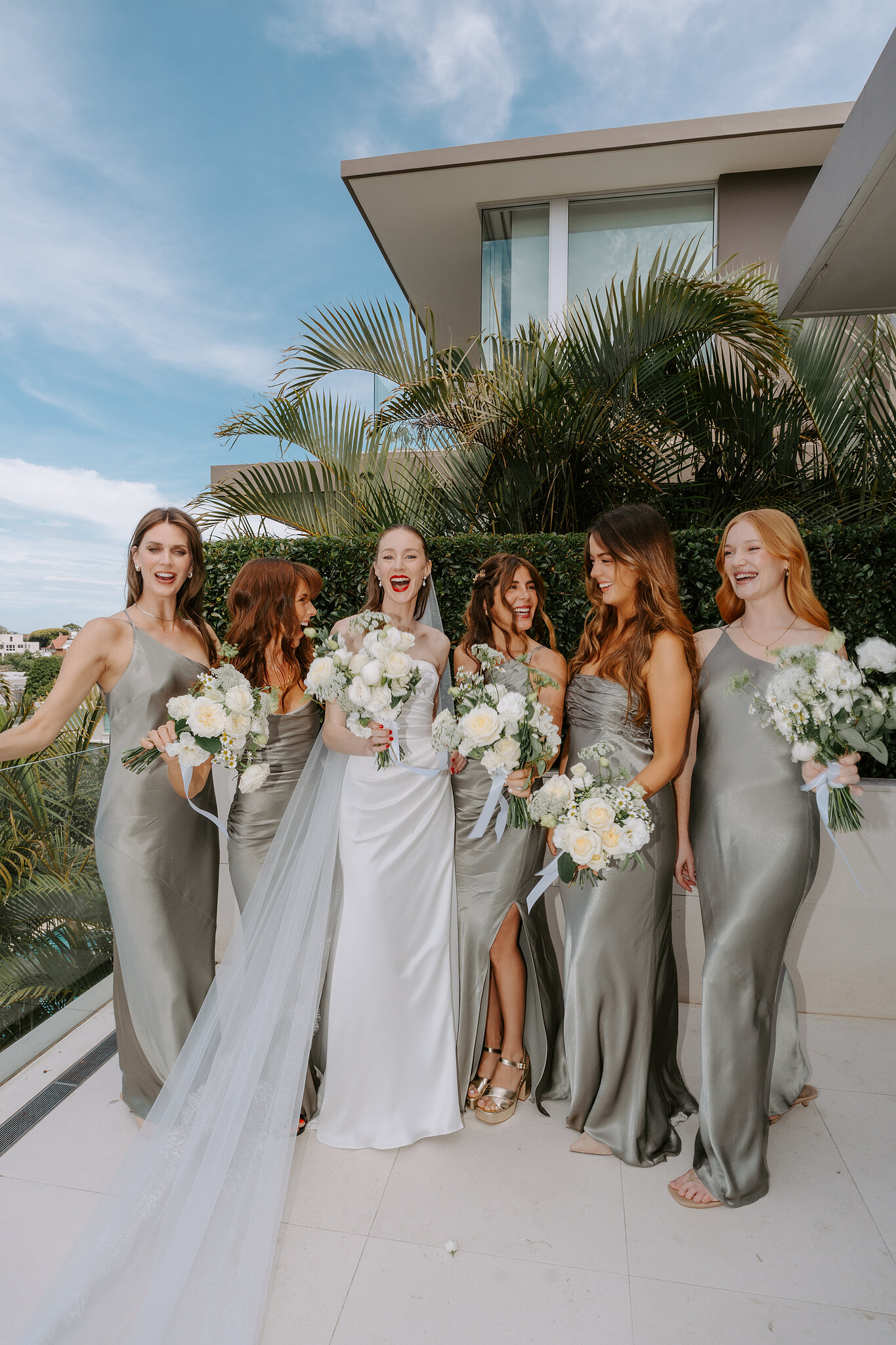 Michele laughing with her five bridesmaids in sage satin, white bouquets in hand, on the terrace.