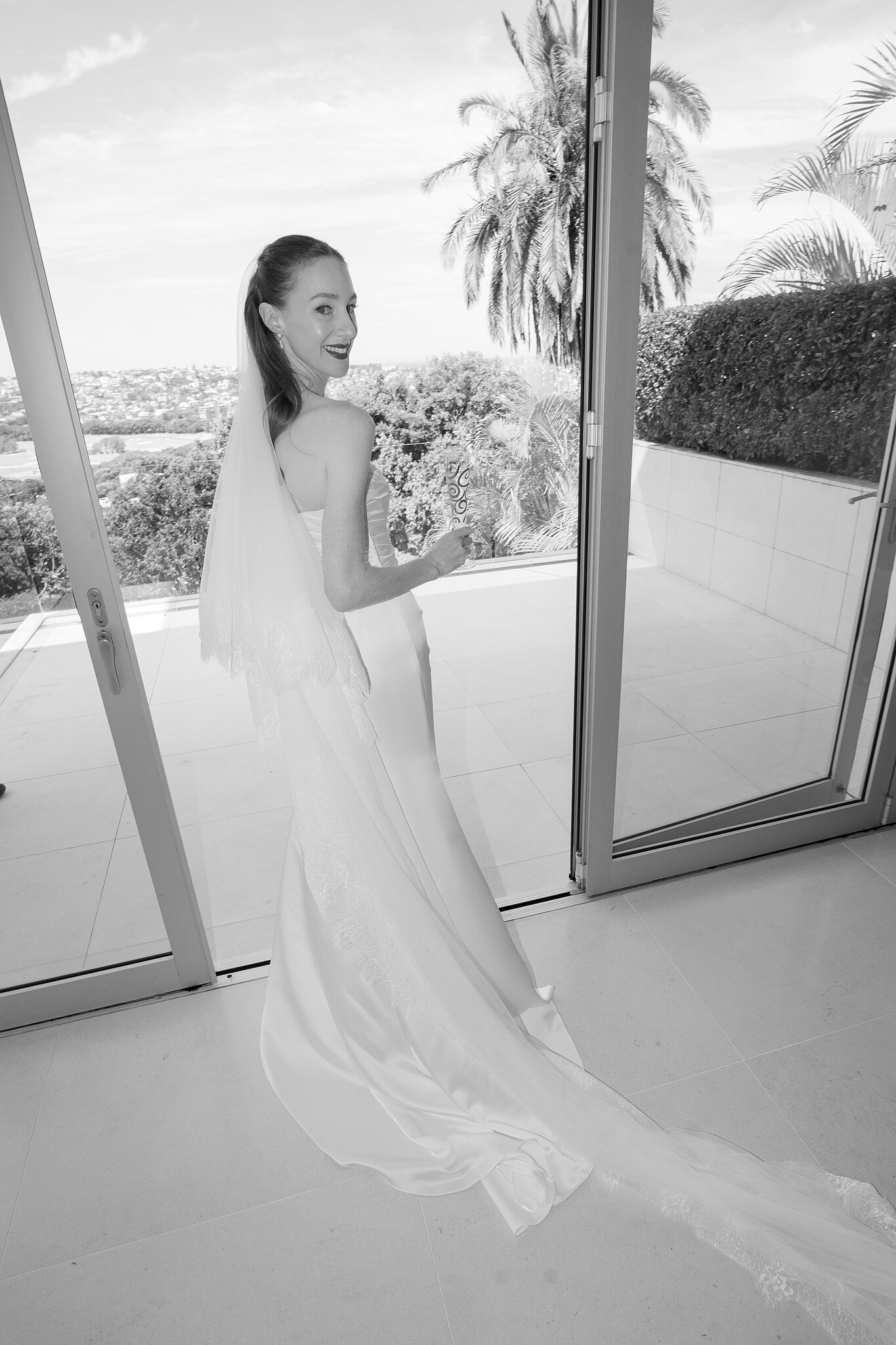 Michele glances back over her shoulder at the terrace door, veil trailing behind her.
